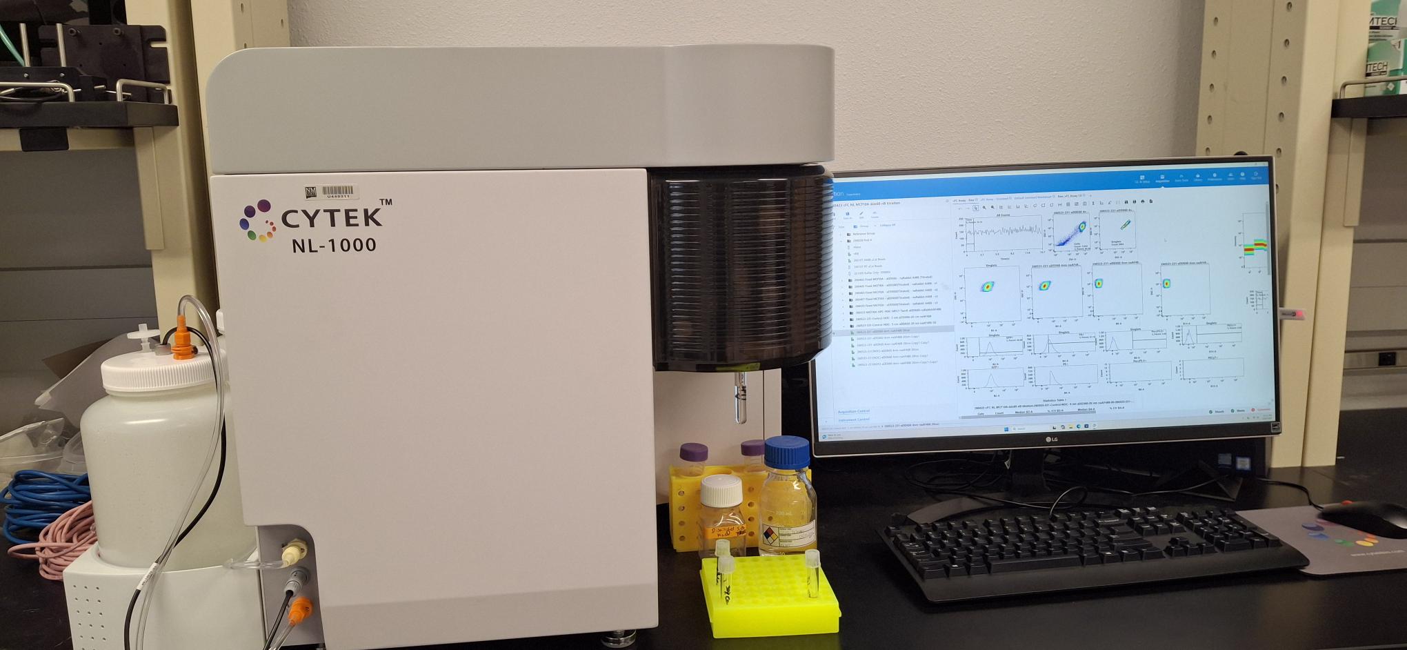 CYTEK NL-1000 laboratory instrument on a bench next to a computer monitor displaying data plots and analysis software.